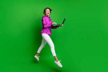 Full body photo of charming astonished active lady jumping use laptop empty space isolated on green color background