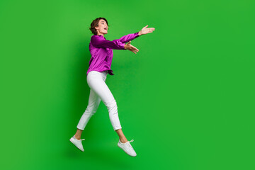 Full length profile photo of crazy cheerful person jump run raise arms catch empty space isolated on green color background