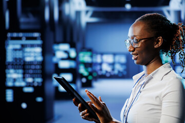 Carefree admin in high tech workspace uses tablet to prevent system overload. Meticulous expert between server units ensuring enough network bandwidth for smooth operations