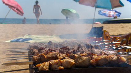 Meat is grilled on the seashore. In the background the sea, beach, umbrellas