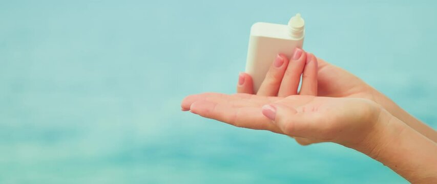 Woman holds a white jar a cosmetic product in hands and dropping liquid into her palm on sea water ripple background. Copy space for text.