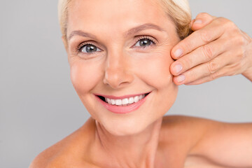 Close up photo of pensioner woman touch under eye skin apply hydrating cream balm isolated on grey...