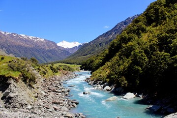 Fototapeta na wymiar New zealand river blue water with green rocks and mountains with snow