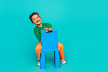 Full length photo of positive glad boy wear trendy green clothes sitting on chair empty space...