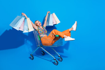 Full length photo of nice girl riding fast on shopping cart with shopping bags in hands on black...