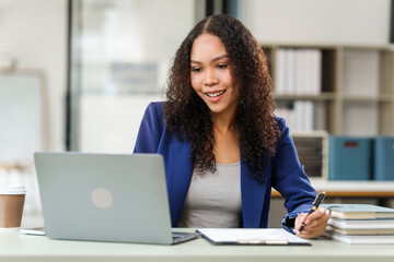 African American university woman working on a project, using a laptop and taking notes, looking...