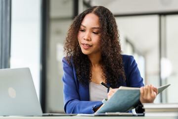 African American university woman working on a project, using a laptop and taking notes, looking...