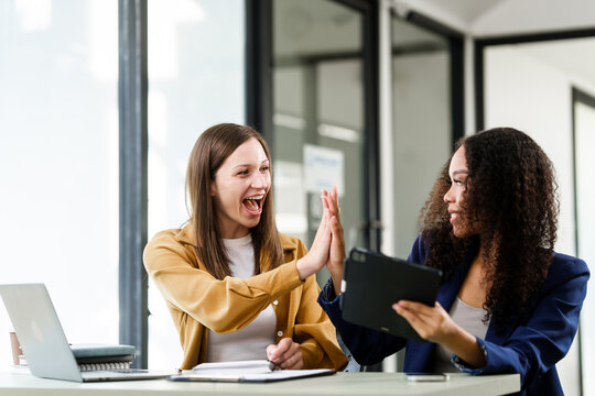 Caucasian and an African American university woman giving a high-five, celebrating a successful project collaboration.