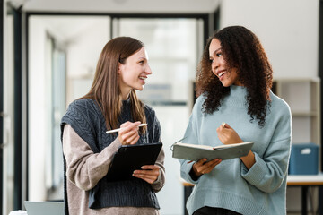 Caucasian and an African American university woman working together on a project, discussing and taking notes.