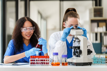 African American and a Caucasian researcher conducting a blood lab test, examining samples with a microscope in a medical laboratory.