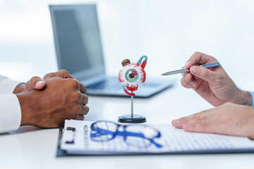 Distressed man meeting doctor, possibly indicating discomfort, while doctor gestures towards model of human eye, perhaps explaining medical condition.