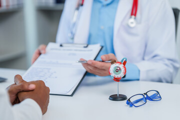 Distressed man meeting doctor, possibly indicating discomfort, while doctor gestures towards model of human eye, perhaps explaining medical condition.