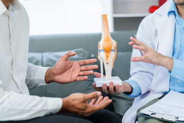 male patient and male doctor discussing a model of a knee joint, likely focusing on condition of knee arthritis during a medical consultation.