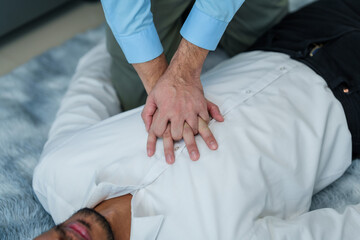 Close up man lying down while another individual, likely a medical professional, is performing a CPR chest compression, potentially in response to heart attack.