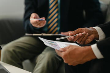 Two men in professional attire on sofa, discussing business matters such as investments or legal topics.