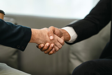 close-up of two men in business suits shaking hands, likely concluding a discussion or agreement,...