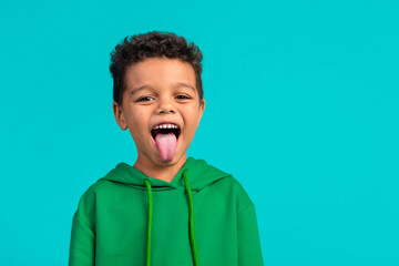 Photo of good mood positive funky schoolboy with wavy hair dressed green pullover stick out tongue...