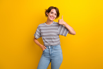 Photo of satisfied nice woman dressed striped t-shirt showing thumb up good work arm in pocket isolated on yellow color background