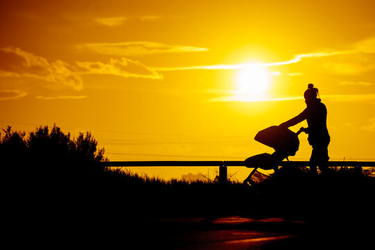 Silhouette of woman with baby stroller walking on beach at sunset