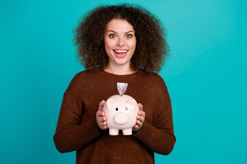 Fototapeta na wymiar Photo portrait of pretty young girl excited hold piggy bank account wear trendy brown outfit isolated on cyan color background
