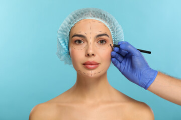 Doctor with pencil preparing patient for cosmetic surgery operation on light blue background