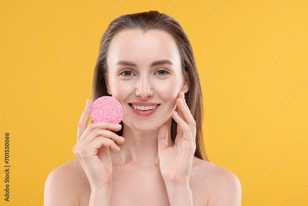 Wall mural Happy young woman washing her face with sponge on orange background