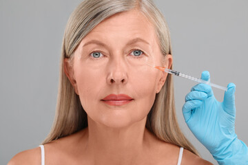 Doctor giving facial injection to senior woman on light grey background, closeup. Cosmetic surgery