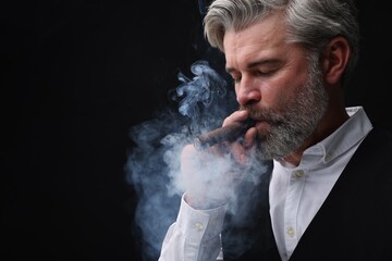 Bearded man smoking cigar against black background. Space for text