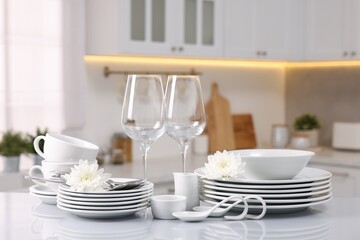 Set of clean dishware, glasses, cutlery and flowers on table in kitchen