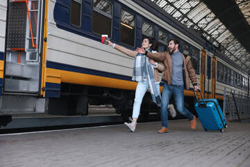 Being late. Worried couple with suitcase running towards train at station