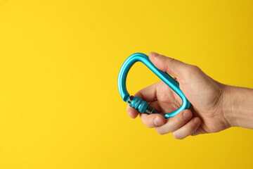 Man with metal carabiner on yellow background, closeup. Space for text
