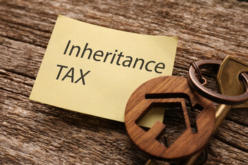Inheritance Tax. Paper note and key with key chain in shape of house on wooden table, closeup