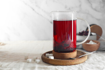 Delicious hibiscus tea in teapot and sugar cubes on table. Space for text