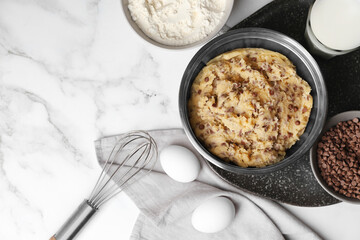 Chocolate chip cookie dough in bowl and ingredients on white marble table, flat lay. Space for text