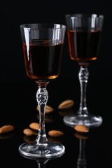 Liqueur glasses with tasty amaretto and almonds on black table, closeup