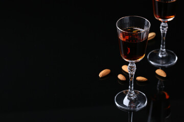 Liqueur glass with tasty amaretto and almonds on black table. Space for text