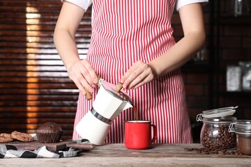 Woman pouring aromatic coffee from moka pot into cup at wooden table indoors, closeup