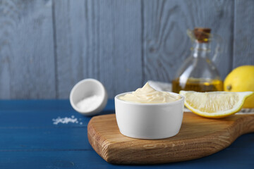 Fototapeta na wymiar Tasty mayonnaise in bowl and lemon wedge on blue wooden table, space for text