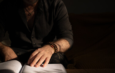 Adult man reading on sofa with bracelets on wrist and necklace on neck