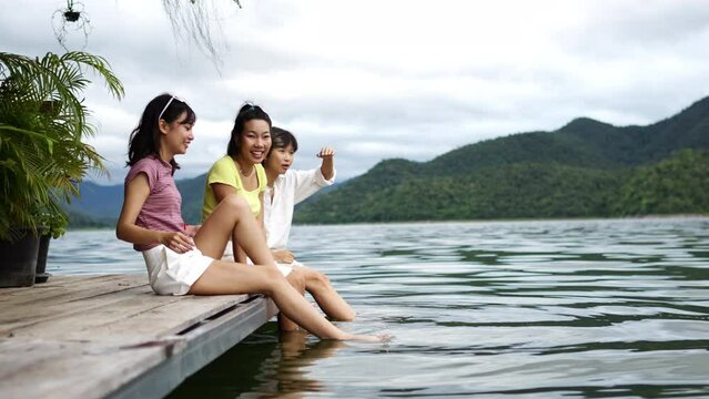 4K Group of Young Asian woman sitting on lake house balcony with splashing legs in water and talking together. People enjoy and fun outdoor lifestyle travel nature mountain on summer holiday vacation
