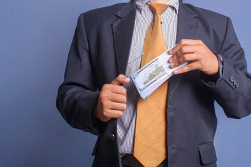 Man in suit putting bribe money into pocket on blue background, Concept for corruption, finance...