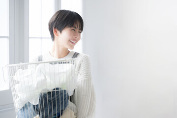 逆光の窓辺で洗濯物を持つ女性の横顔上半身　ライフスタイルの家事や爽やかな主婦のイメージ © kapinon