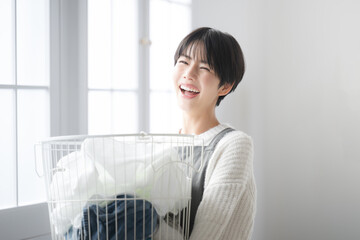 Top half of woman looking at camera holding laundry by window Image of lifestyle housework and fresh housewife backlighting - obrazy, fototapety, plakaty