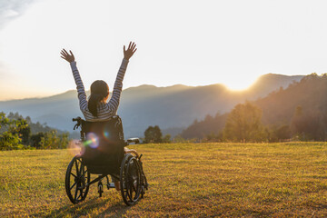 Person sitting on a wheelchair enjoying with raised hands on the mountain at the sunset time.