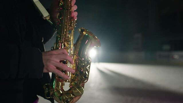 Slowmotion of saxophone player playing a song on a snow covered winter stadium with ice skaters in background