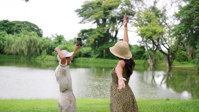 4K Happy Asian LGBTQ people enjoy outdoor lifestyle travel nature on summer holiday vacation. Lesbian couple using mobile taking selfie together at outdoor cafe.  LGBT person and pride day concept.