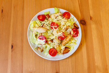 Fresh healthy caesar salad with chicken breast, cherry tomatoes, lettuce, parmesan cheese, dressing and croutons on wooden table. Top view