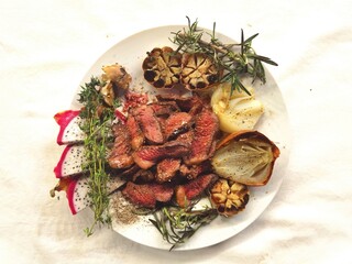 Top view of grilled sliced steak and rosemary on white plate