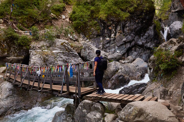 Tourists walk on a suspension bridge over a mountain river. Extreme outdoor recreation in the...
