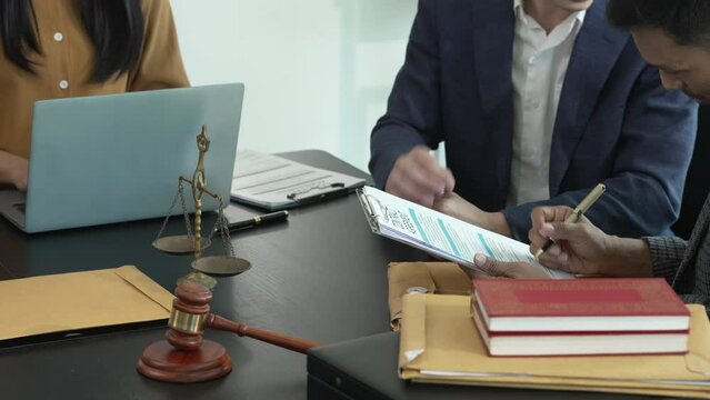 Asian legal team in meeting. woman and two men discussing over documents with law books and gavel on the table, indicating legal setting.